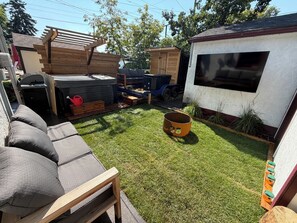 Un patio trasero con terraza de madera, una parrilla, un jacuzzi y un cobertizo.