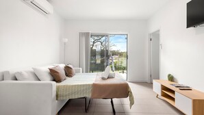 Ein modernes, minimalistisches Schlafzimmer mit Bett, Sofa, Fernseher und einer Schiebeglastür zum Balkon.