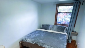 A small, well-lit bedroom with a single bed, a window with a view, and a wooden floor.