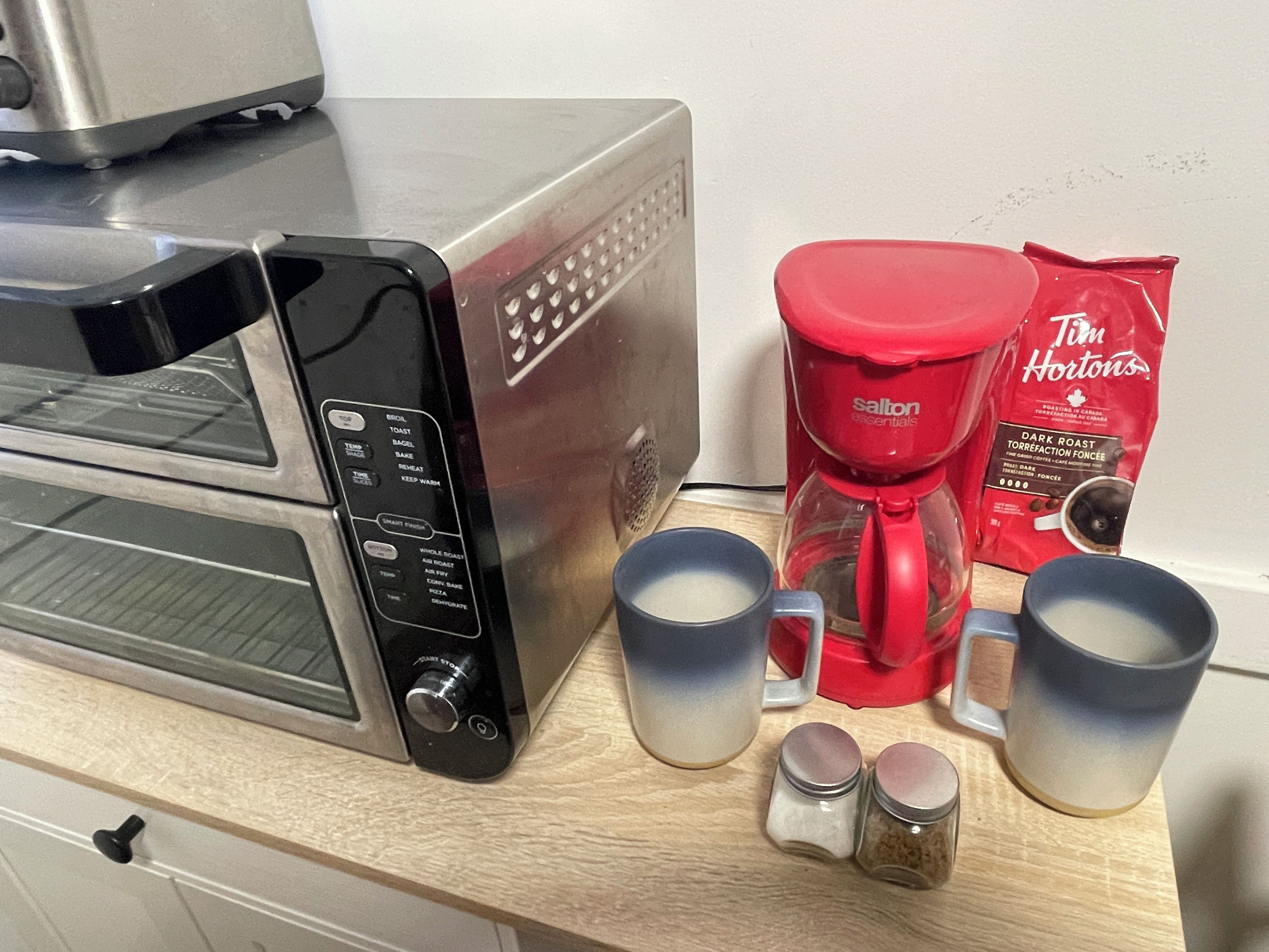 A kitchen with a toaster oven, a red coffee maker, and two mugs.