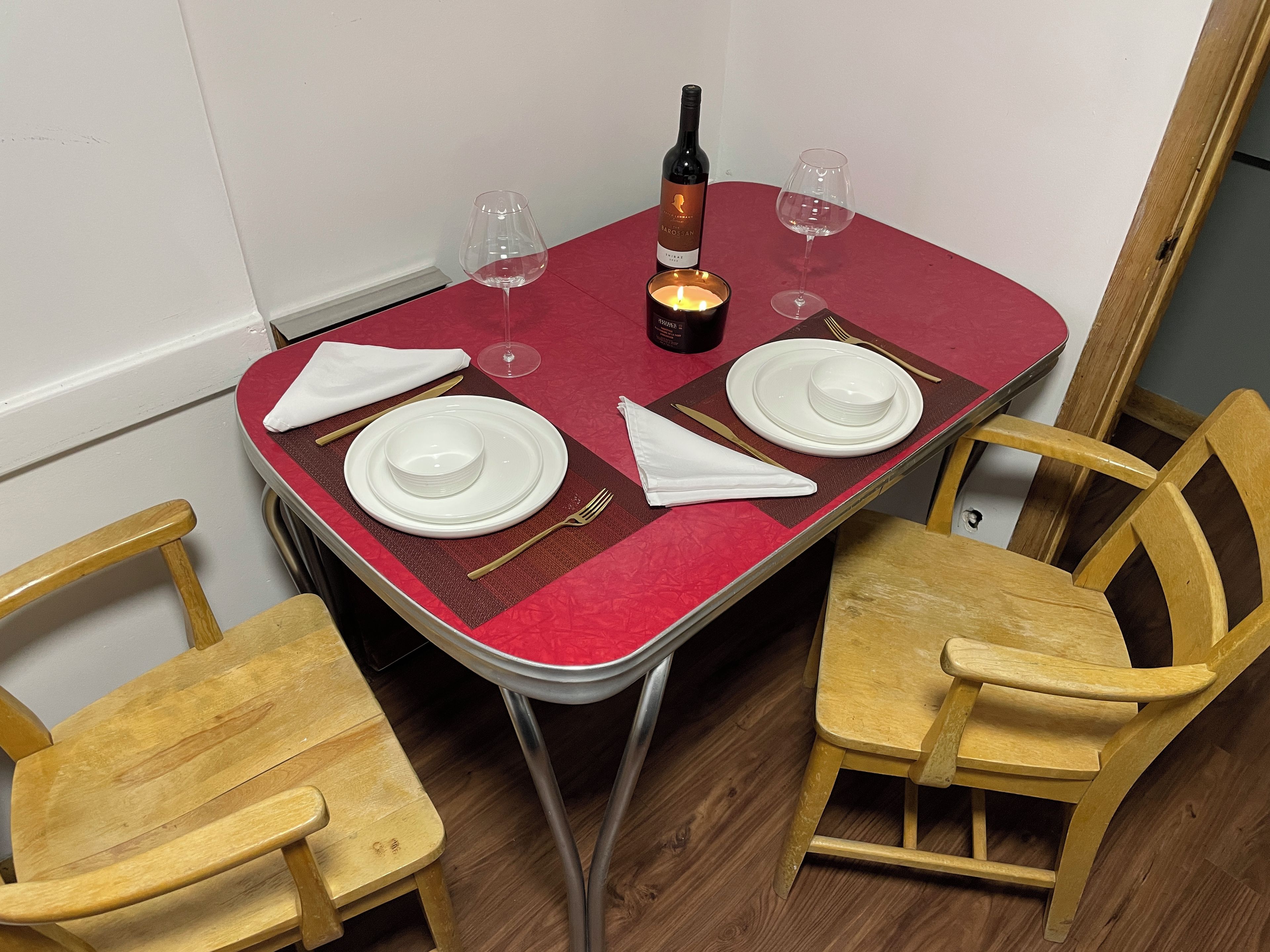 Une table à manger recouverte d’une nappe rouge, avec deux assiettes blanches, une bouteille de vin et deux verres.