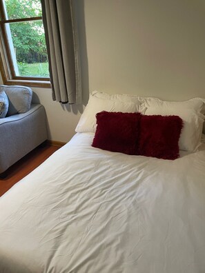 Una camera da letto con un letto, una poltrona grigia e una finestra con tende.