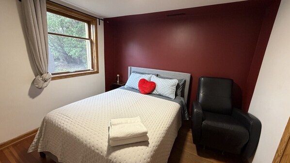 A bedroom with a bed, a chair, a window, and a red wall.