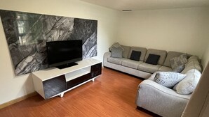 A living room with a flat-screen TV on a white stand, a grey sofa with patterned cushions, and a marble wall. - Welcome to the Cabernet Escape– A Bold, Wine-Inspired Urban Escape (Calgary)