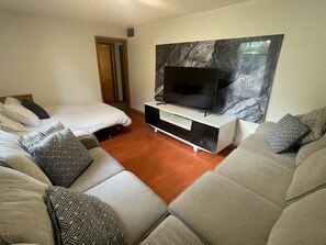 A modern living room with a large flat-screen TV mounted on a marble wall, a sofa set with patterned cushions, and a wooden floor.