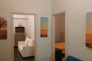Um corredor com um sofá branco, um pequeno armário com garrafas e um quadro na parede.