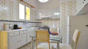 A compact kitchen with white cabinets, a glass table, and a chair.