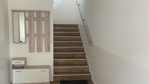 Una escalera de madera con barandilla de metal, que conduce a un rellano con una consola blanca y un espejo.