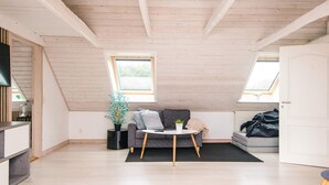 A loft-style room with a sloped ceiling, two skylights, a grey sofa, a small round table, and a potted plant. - 4 Star Holiday Home in Henne (Henne)