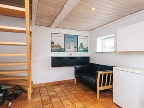 A room with a black leather sofa, a white refrigerator, a wooden shelf, and a tiled floor. - 4 Star Holiday Home in Henne (Henne)