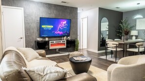 A modern living room with a leather sofa, a flat-screen TV, a fireplace, and a dining area with a table and chairs. - Cozy 3b2b Duplex Home in South Austin (Austin)