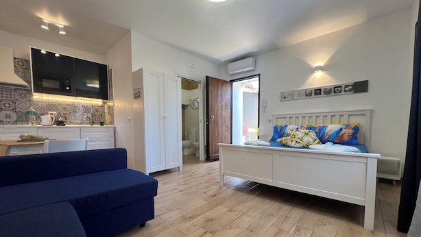 A modern bedroom with a bed, a blue sofa, a kitchen area with a microwave, and a tiled backsplash. - [ Duomo Delight ] + Self Check-in Late (Catania)