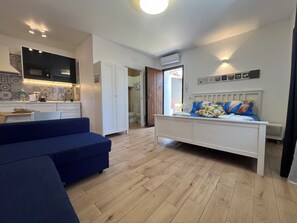 A modern bedroom with a bed, a blue sofa, a kitchen area with a microwave, and a tiled backsplash. - [ Duomo Delight ] + Self Check-in Late (Catania)