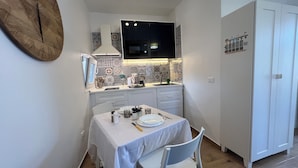 A compact kitchen with a dining area, featuring a white table set with plates, a kettle, and a coffee maker. - [ Duomo Delight ] + Self Check-in Late (Catania)