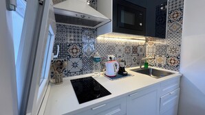 A compact kitchen with a microwave, kettle, and coffee maker on the counter, a sink, and a stove with a hood. - [ Duomo Delight ] + Self Check-in Late (Catania)