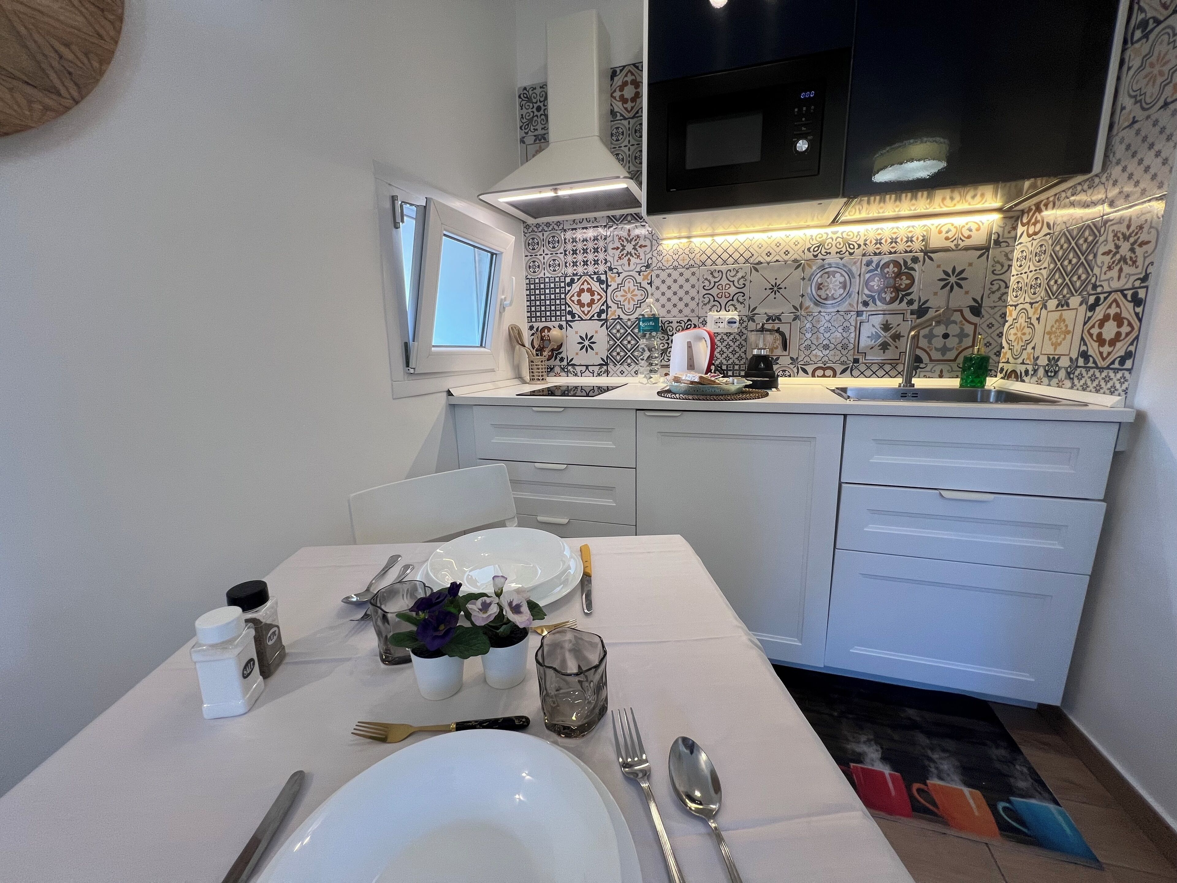 A kitchen with a dining area, white cabinets, a microwave, and a window.