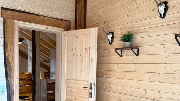 A wooden interior with a wooden door, a wall-mounted shelf with a plant, and a wooden cabinet. - Chalet on the Wolfsberg (Harzgerode)