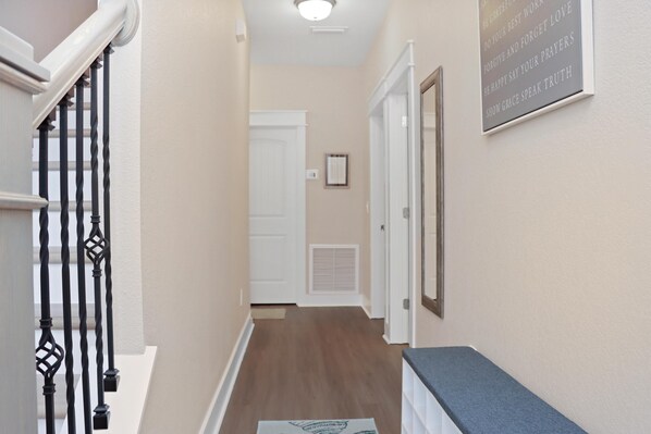 A hallway with a wooden floor, a staircase with black balusters, and a wall-mounted sign with inspirational quotes.