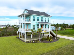 Une maison à deux étages dotée d’un balcon et d’un porche abrité, entourée d’une pelouse et de palmiers.