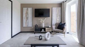 Una sala de estar moderna con un televisor de pantalla plana, arte abstracto en la pared, un sofá, una mesa de centro y un amplio ventanal con cortinas.
