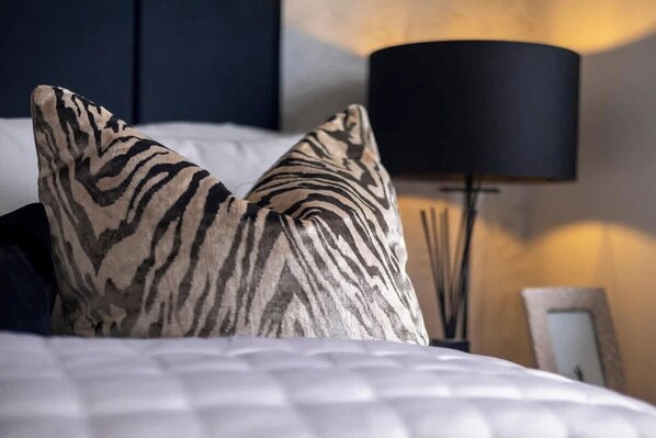 A bed with zebra-patterned pillows, a black lamp, and a framed picture on the wall.