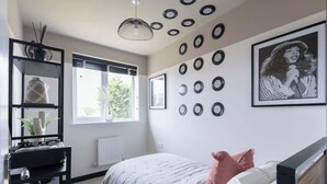Un dormitorio con cama, un escritorio con computadora, una ventana y adornos en las paredes, incluyendo cuadros y discos de vinilo.