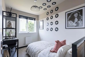 A bedroom with a bed, a desk with a computer, a window, and wall decorations including framed pictures and vinyl records.