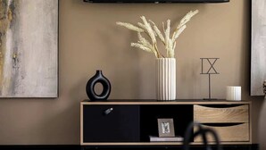 Un salón moderno con diseño minimalista, que incluye un mueble de madera, un florero negro y un florero blanco con plantas secas.