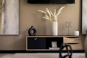Un salón moderno con diseño minimalista, que incluye un mueble de madera, un florero negro y un florero blanco con plantas secas.