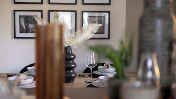 Una mesa de comedor con un florero, una pluma, una copa de vino y platos.