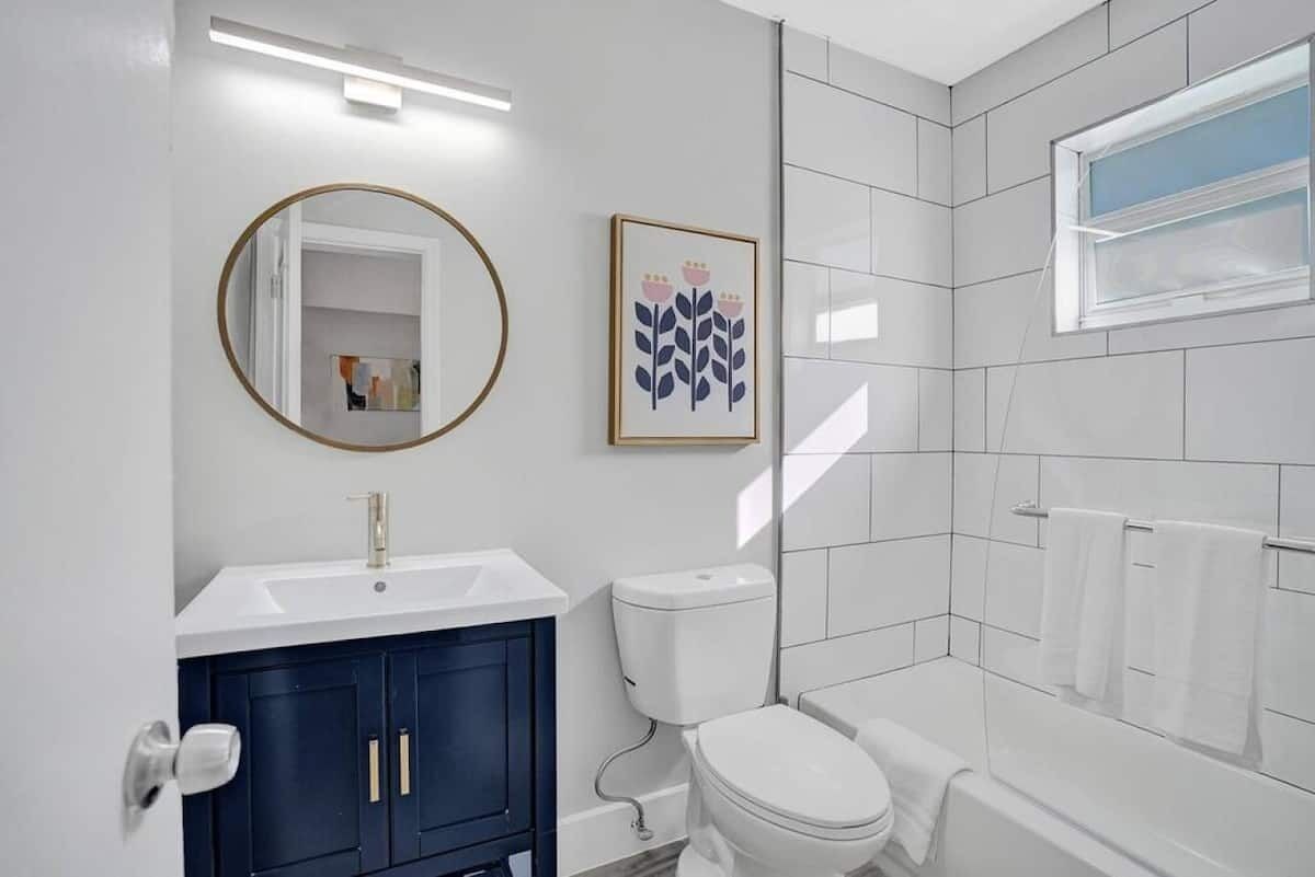 Une salle de bain moderne avec un lavabo blanc, des meubles bleu foncé, des toilettes blanches et une douche à l’italienne en verre.