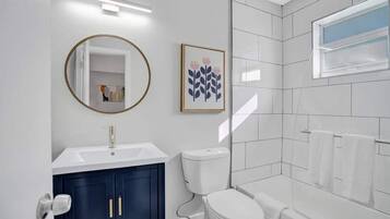 Une salle de bain moderne avec un lavabo blanc, des meubles bleu foncé, des toilettes blanches et une douche à l’italienne en verre.
