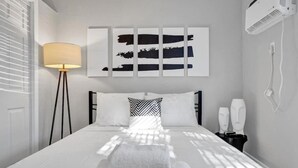 Ein ordentlich bezogenes Bett mit weißen Leinentüchern, einer Nachttischlampe und einem Wandbild.