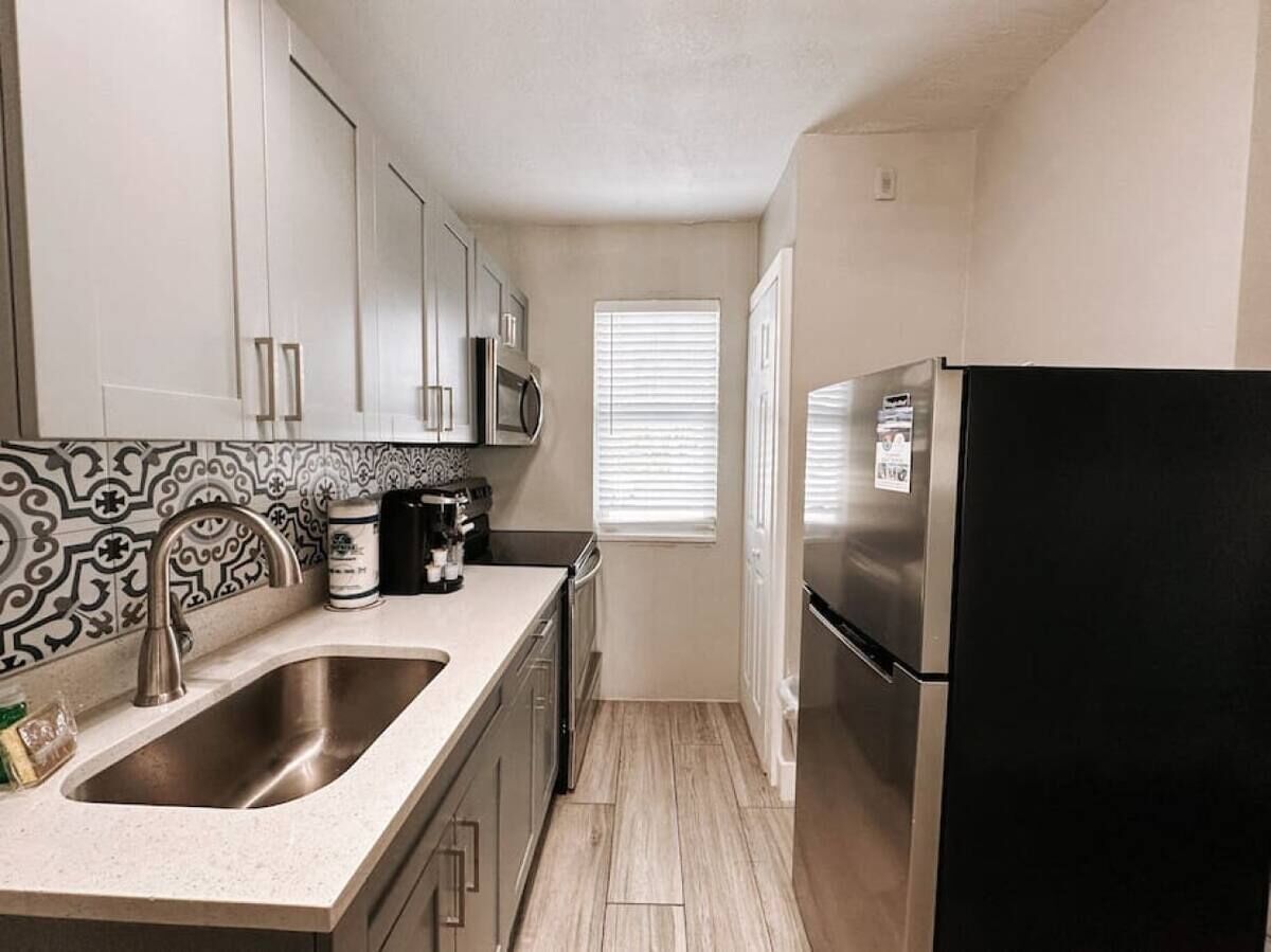 A compact kitchen with a double sink, stainless steel appliances, and a patterned backsplash.