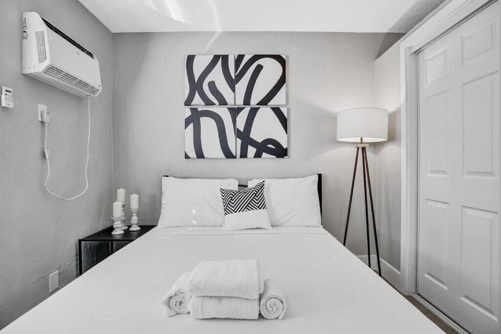 Ein modernes Hotelzimmer mit einem ordentlich bezogenen Bett, einem Nachttisch mit Lampe und einer Wand-Klimaanlage.
