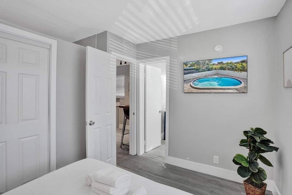 A bedroom with a bed, a potted plant, and a painting of a swimming pool.
