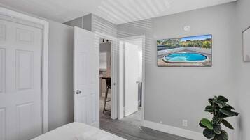 A bedroom with a bed, a potted plant, and a painting of a swimming pool.