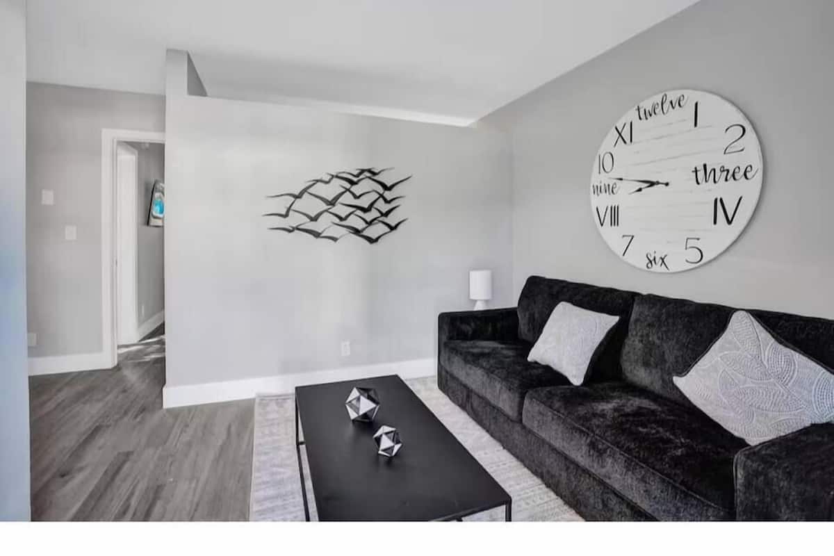 Ein modernes Wohnzimmer mit einer großen Wanduhr, einem dunklen Sofa und einem Couchtisch.