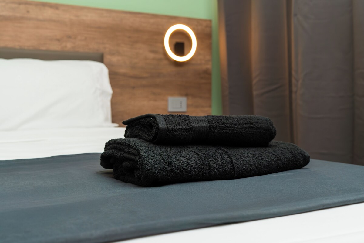 A neatly made bed with a dark gray bedspread and two folded black towels.