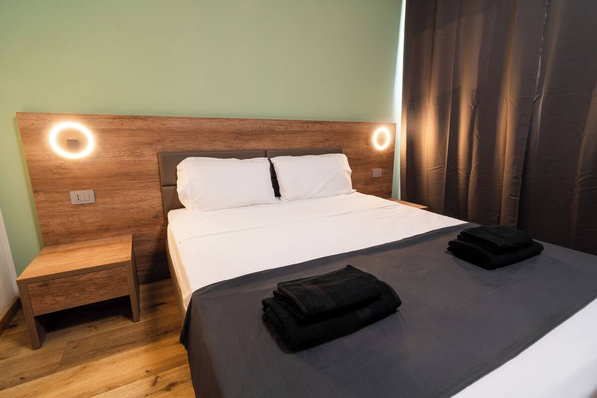 Un lit bien fait, recouvert d’une couverture sombre, avec deux oreillers et deux serviettes pliées posées sur le lit.