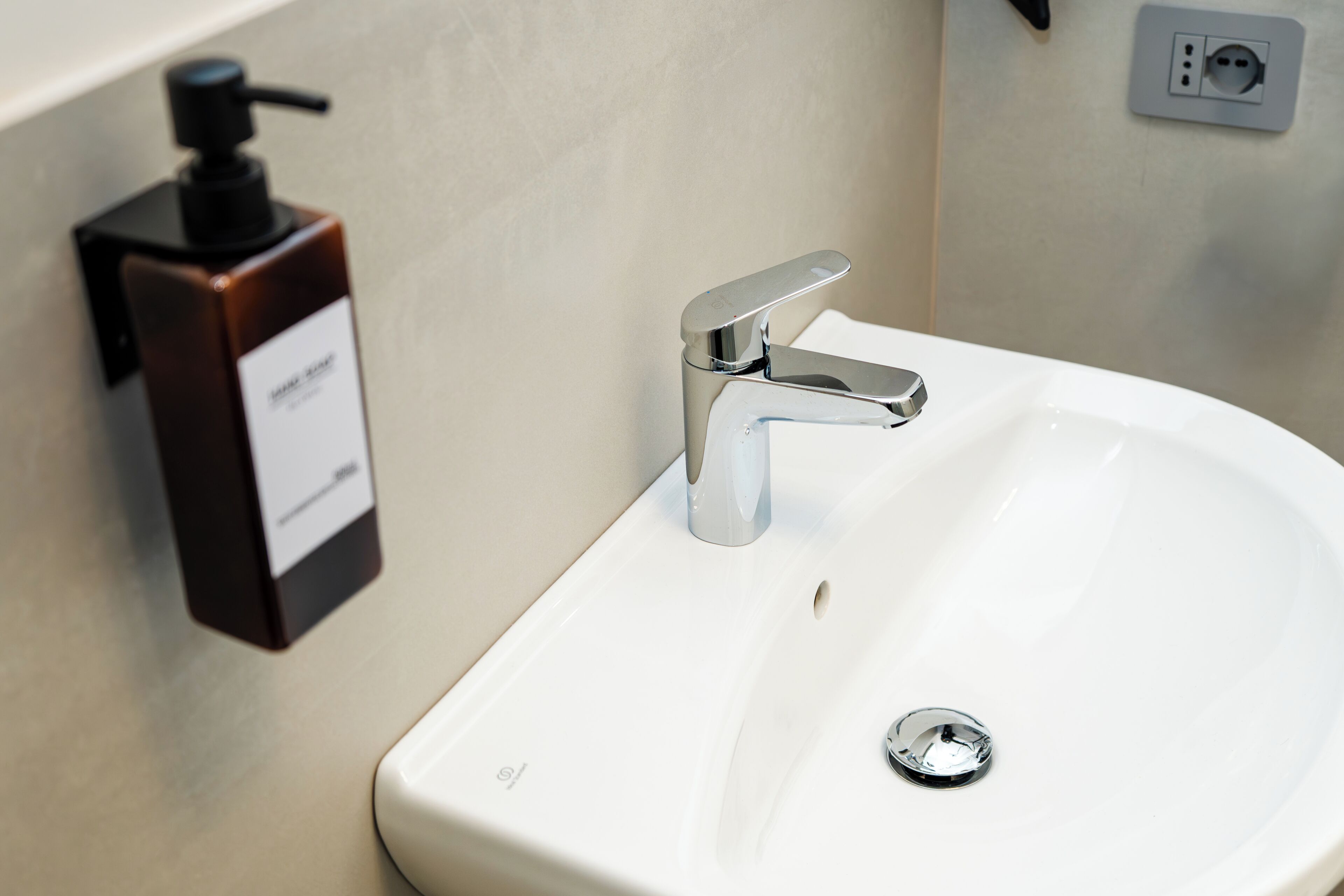 A white bathroom sink with a chrome faucet, a soap dispenser, and a wall socket.