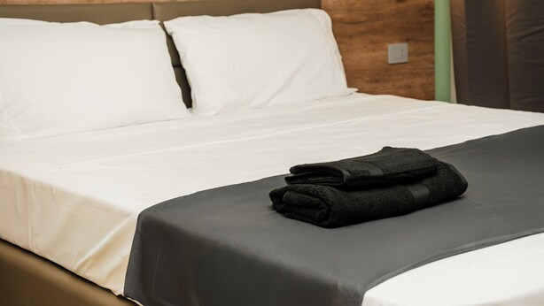 A neatly made bed with white linens and a black blanket, a wooden headboard, and a wall-mounted light fixture. - Elysium Self Check-In Rooms (Trezzo sull'Adda)