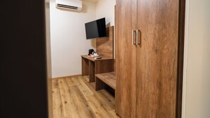 A room with a wooden wardrobe, a desk with a flat-screen TV, and an air conditioning unit on the wall. - Elysium Self Check-In Rooms (Trezzo sull'Adda)