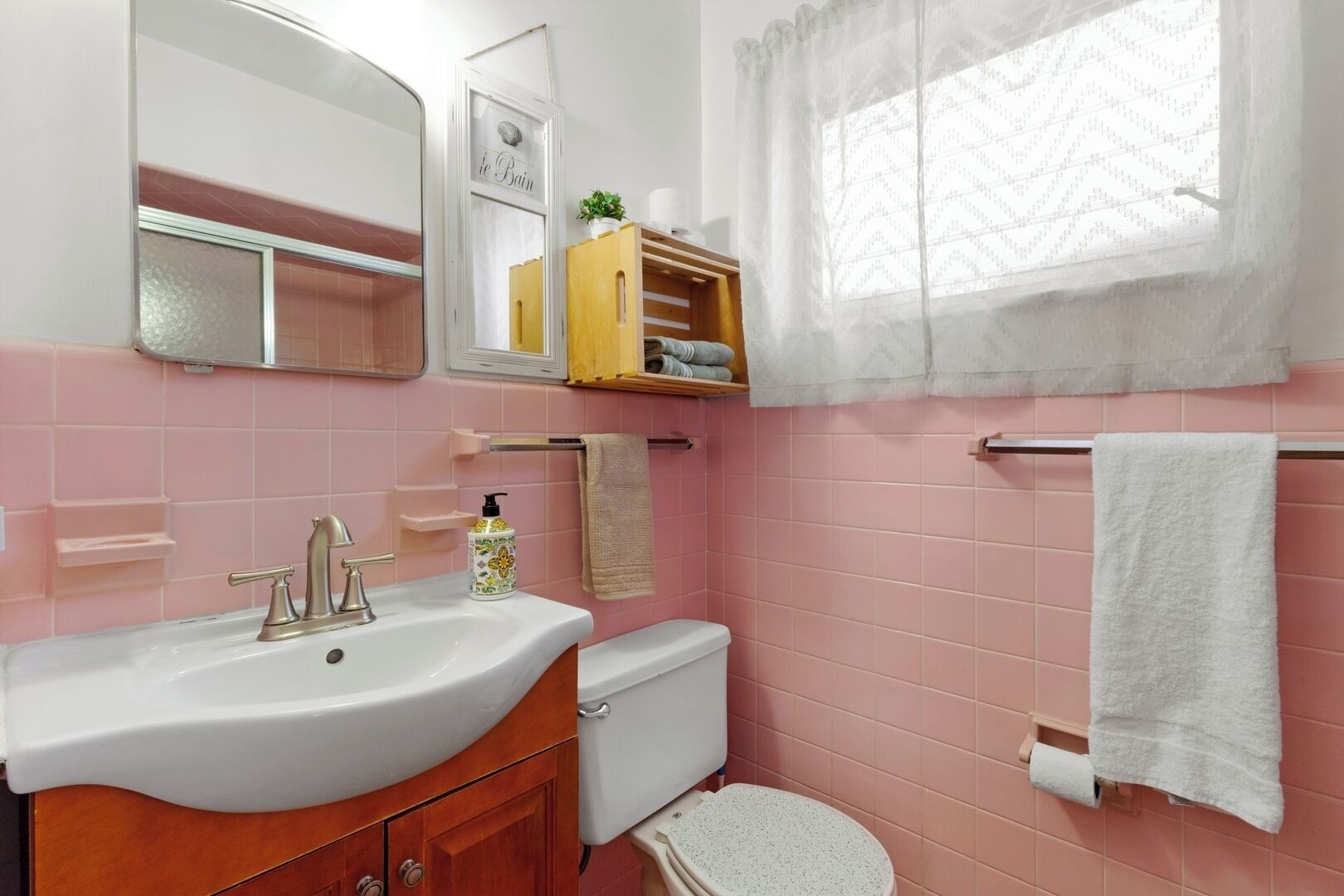 Un baño con azulejos rosas, un lavabo blanco, un inodoro y un espejo.