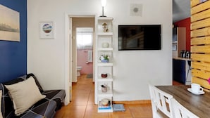 Una sala de estar con un sofá, una mesa de centro, un televisor y una estantería.