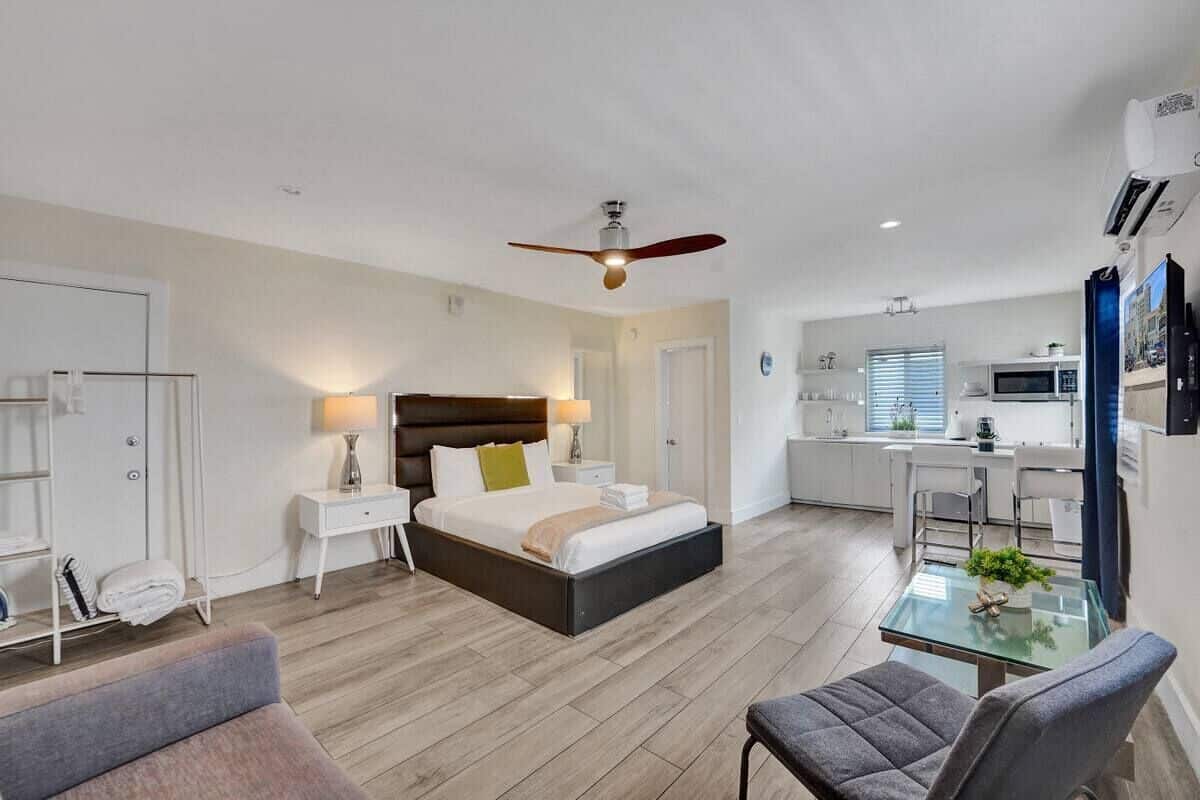 Una habitación de hotel moderna con cama, mesitas de noche, un escritorio y una kitchenette.