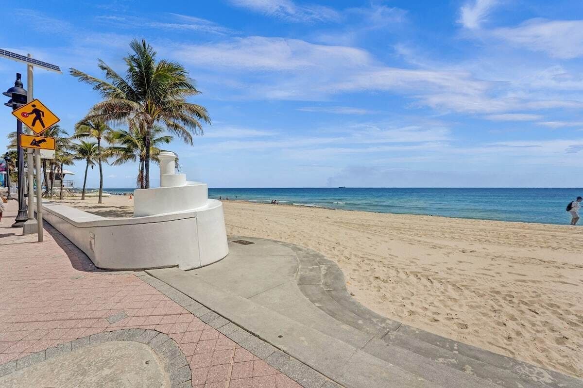 A beach with a white circular structure, palm trees, and a clear blue sky.