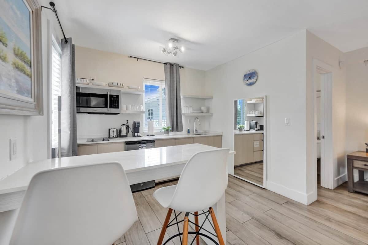 A modern kitchen with white cabinetry, a central island, and a dining area with white chairs.