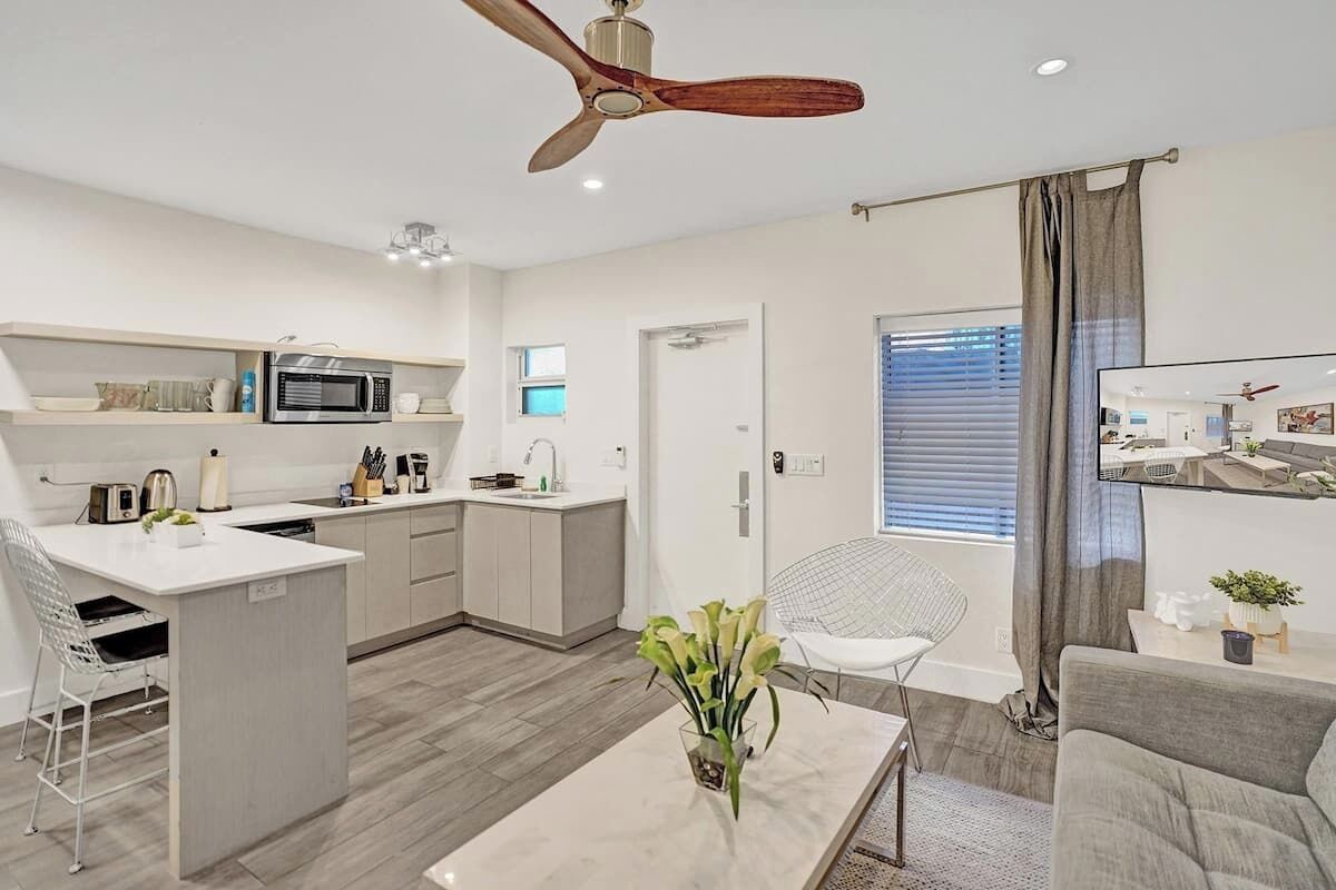 A modern kitchen with a microwave, toaster, and coffee maker. There is a dining area with a white chair and a table.