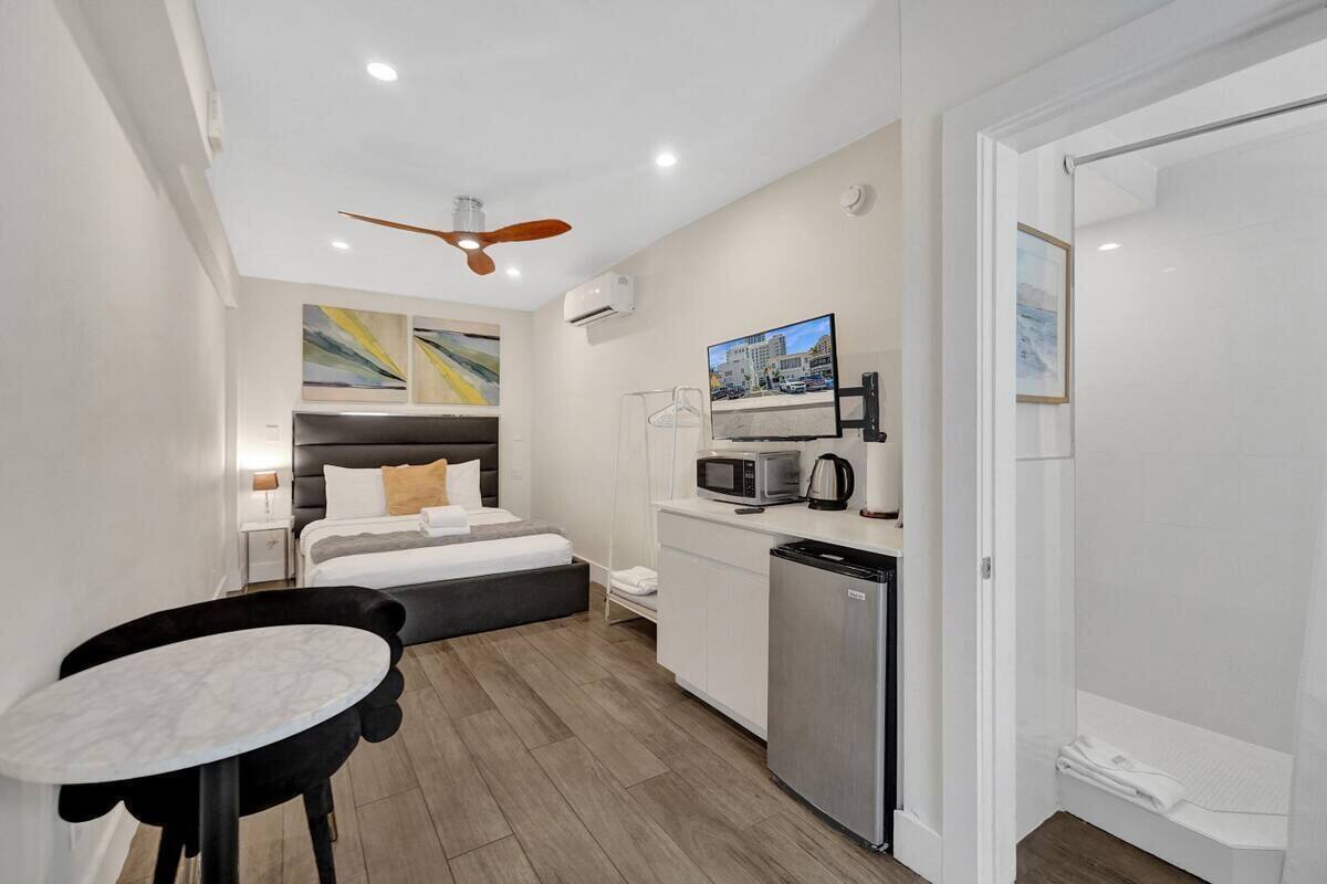 Una habitación de hotel compacta con cama, kitchenette, comedor y ducha.